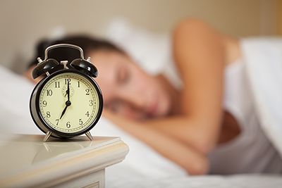 A woan sleeps, with an alrmclock in the foreground